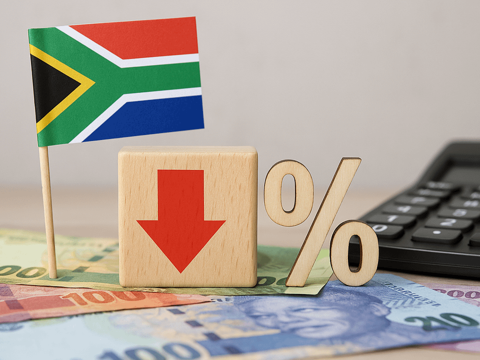 South African flag next to a wooden block with a red downward arrow and a percentage symbol, placed on South African rand banknotes, with a calculator in the background—symbolizing an interest rate cut in South Africa.